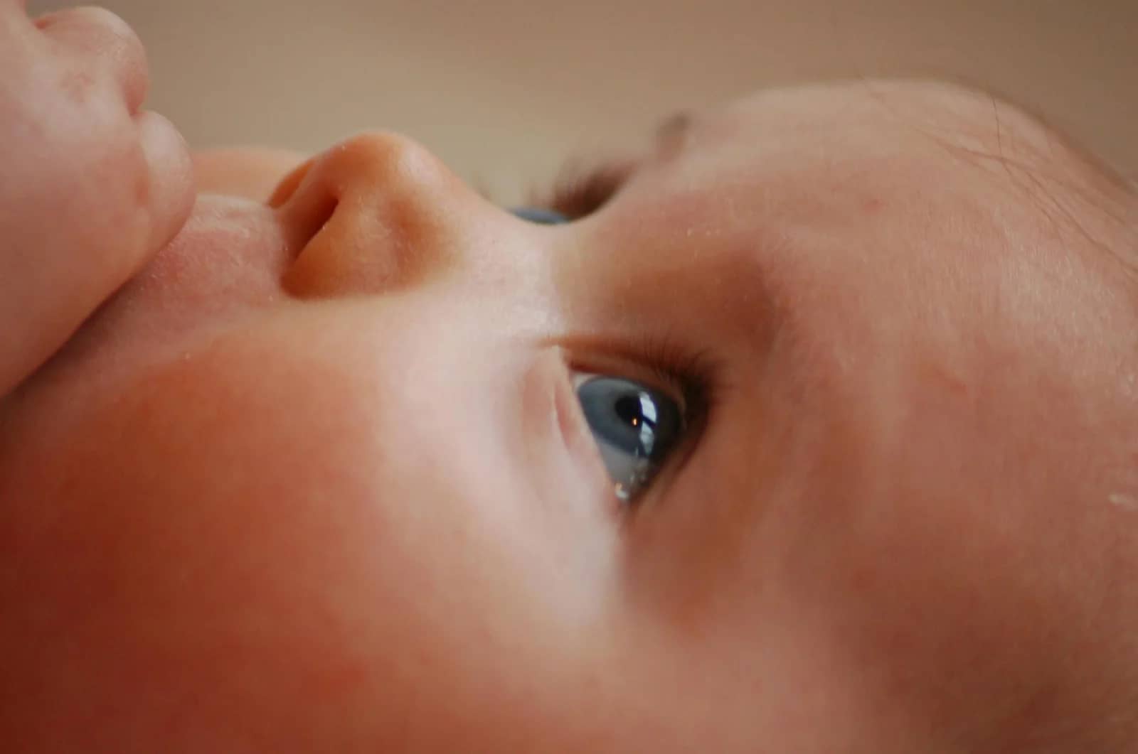 Close-up of a baby's face showing a blue eye and a part of their nose, with soft lighting and smooth skin texture.