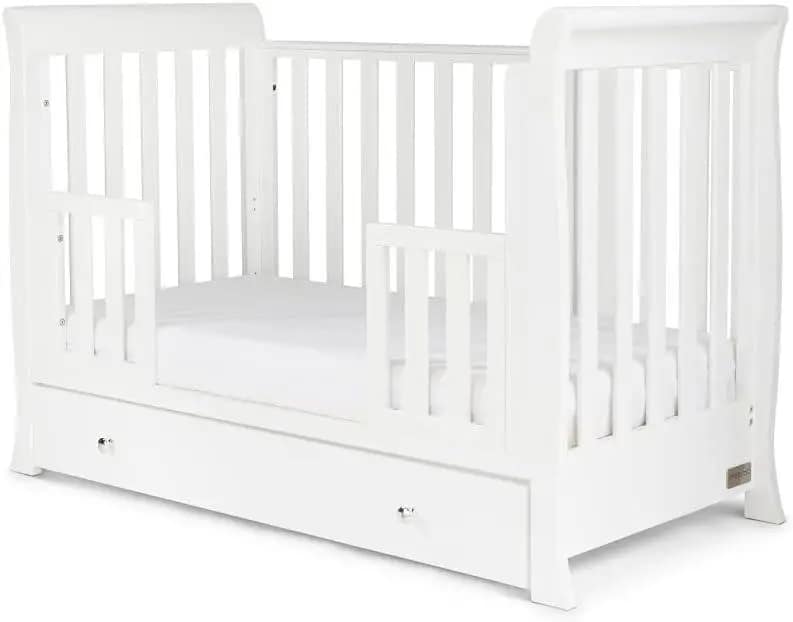 Ickle Bubba Snowdon Mini Cot Bed: A white wooden crib featuring vertical slats, a smooth curved top rail, and a matching under-drawer for storage, with a soft mattress visible inside.