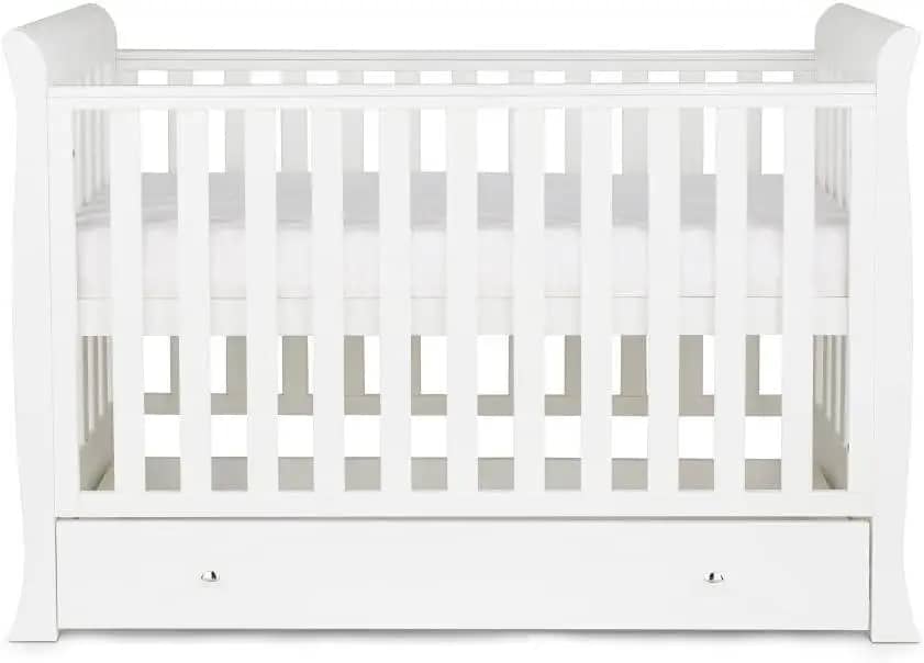 A white wooden crib with slatted sides and a solid base, featuring a storage drawer underneath.